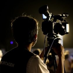 A cameraman filming an event outdoors at night with professional equipment, capturing the vibrant atmosphere.