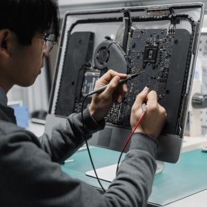 A technician works on a computer motherboard using tools at a workspace, focusing on electronics repair.