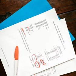 Overhead view of financial documents with red highlighted sections on a wooden desk.